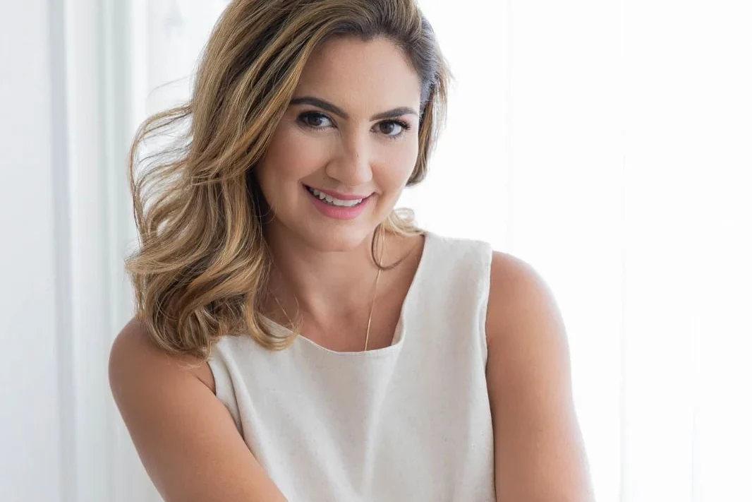 Renata Fantinati sorrindo, sentada, com os braços apoiados nas pernas.