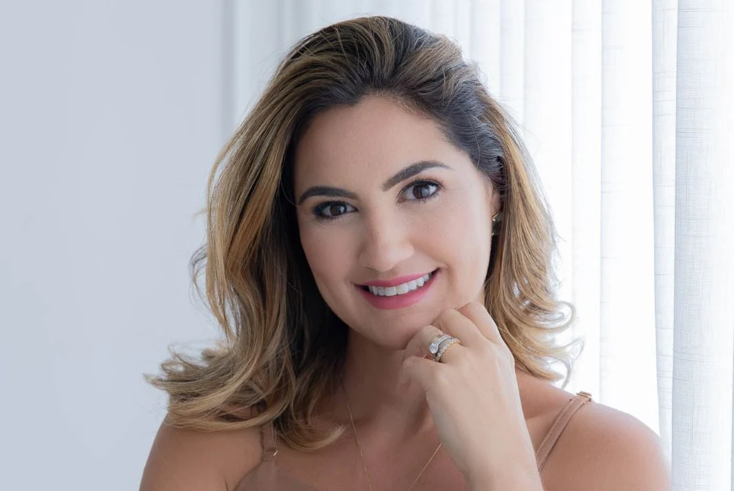 Renata Fantinati sorrindo, com a mão no queixo.